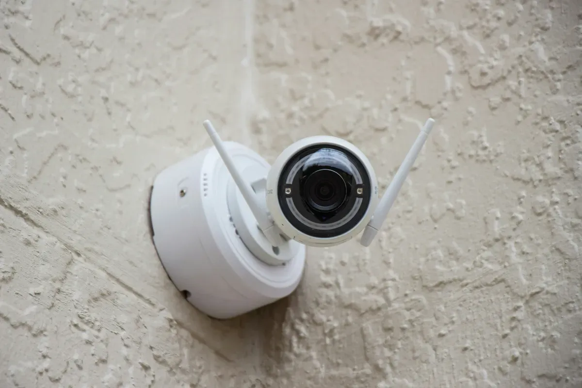 A white surveillance camera hanging from a wall bracket