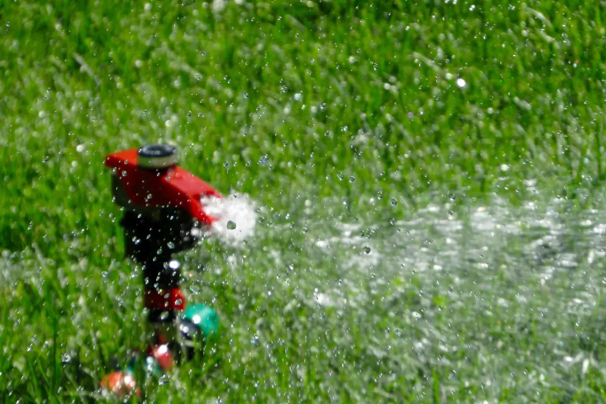 A red garden sprinkler standing on cut grass