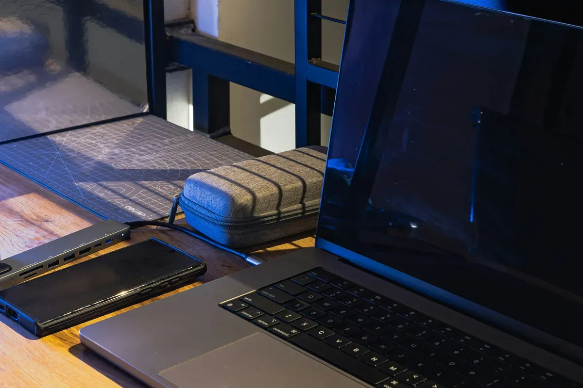 A laptop, phone and charger laid out on a desk at night
