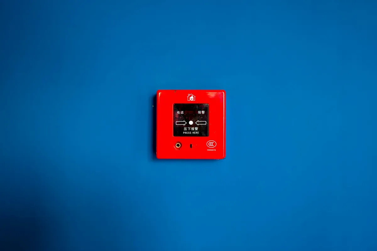 A red alarm call point mounted alone on a blue wall