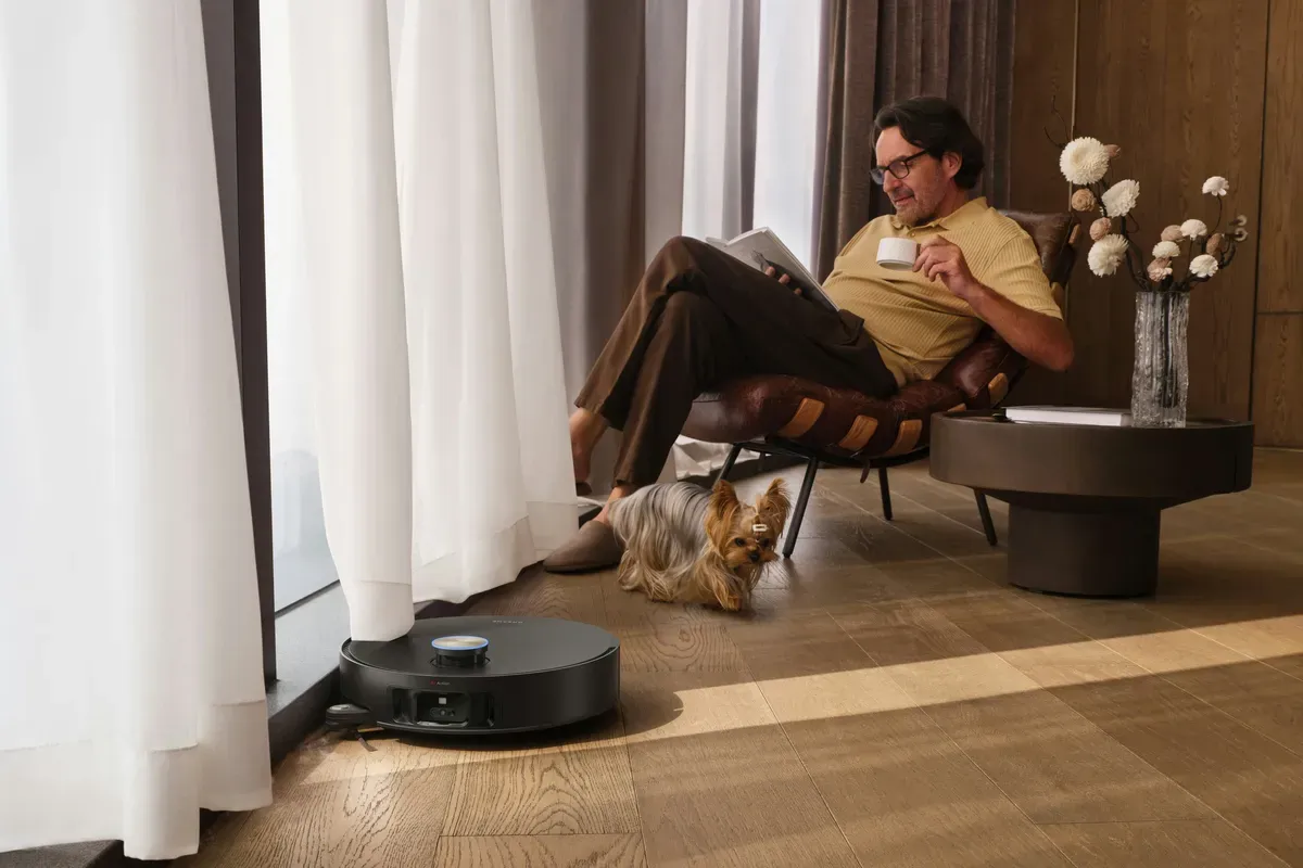 A robot vacuum cleaning a wooden floor near an armchair