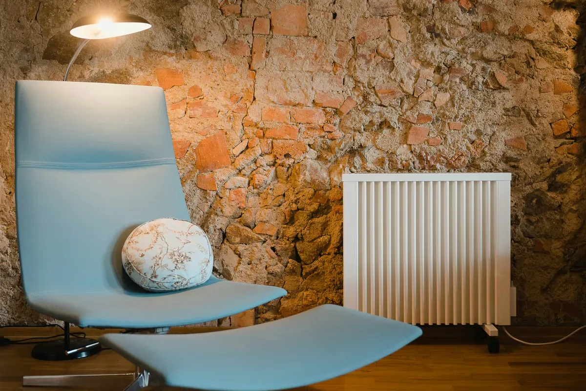 A heater working in a corner of a room beside a chair