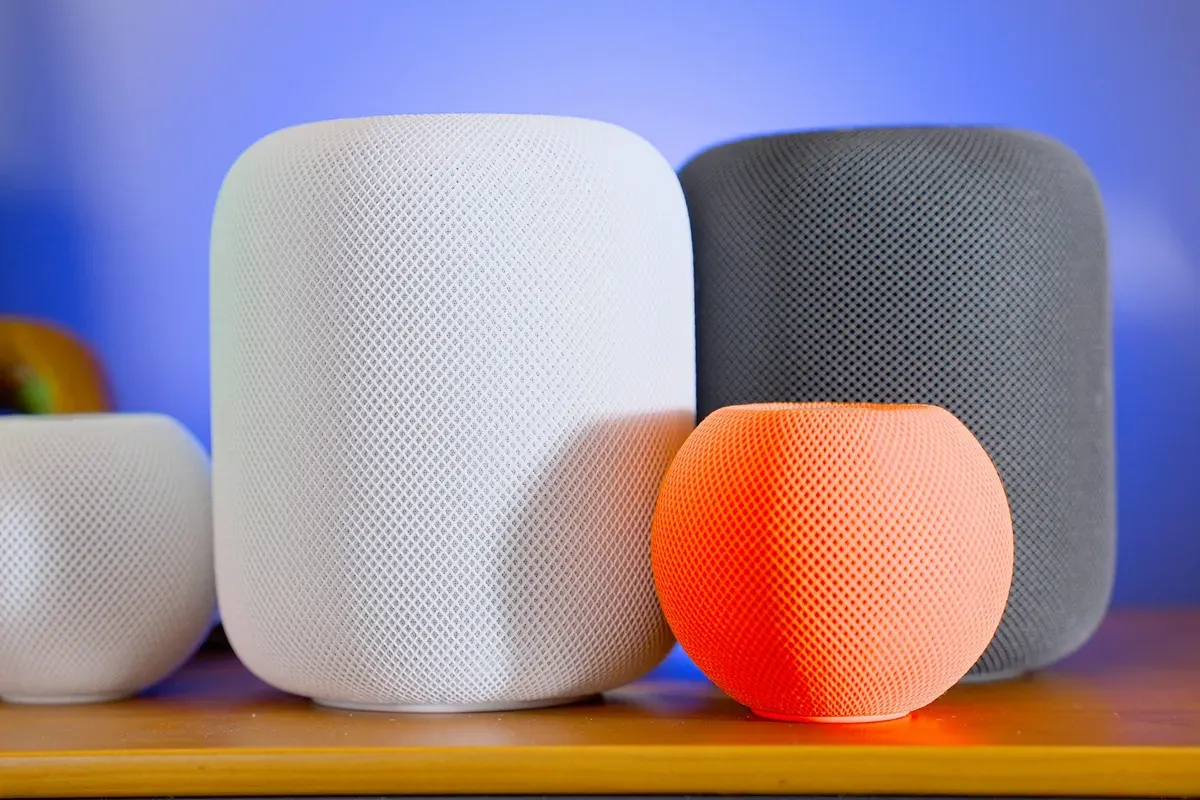 Two HomePods and two HomePod minis, one of them orange, on a wooden shelf
