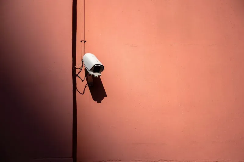White bullet-style CCTV camera fixed to a pale exterior wall in daylight