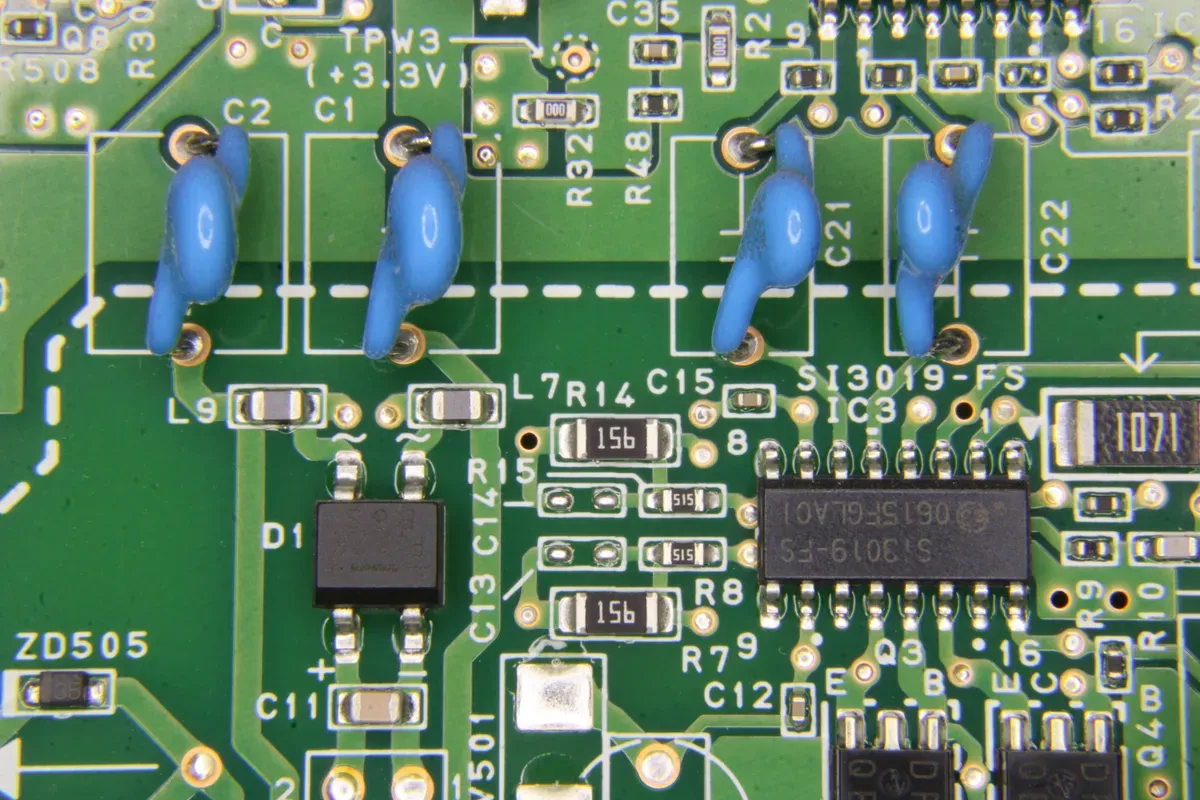 A green circuit board with chips, resistors and blue capacitors