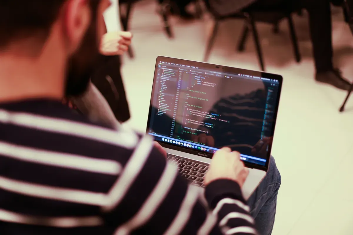 A person at a laptop at a bright table, writing the config by hand