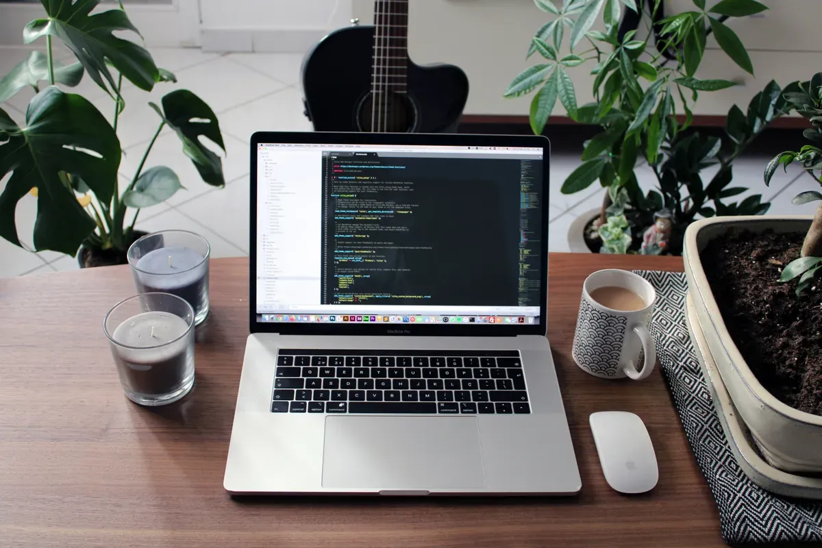 A laptop and mug on a wooden desk with plants behind