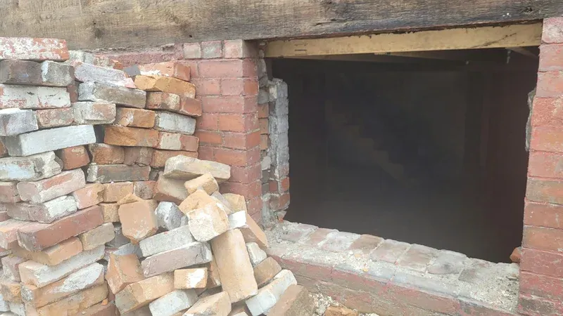 A pile of bricks beside an unfinished opening in a brick wall