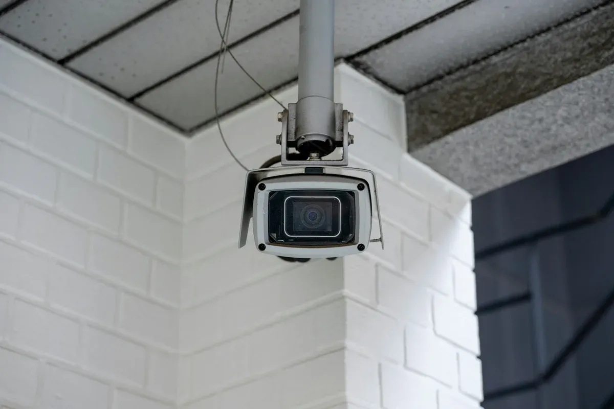 Security camera mounted on a white brick wall, the kind of hardware iOS 27 lets HomeKit record in 4K
