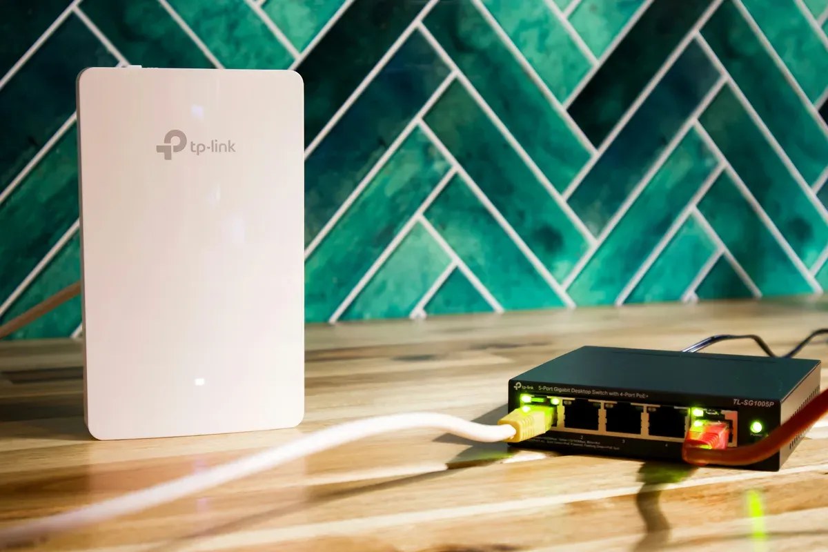 A wireless access point beside a small network switch with patch cables on a wooden surface