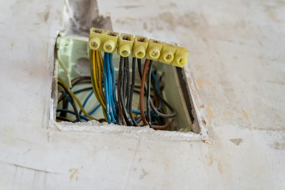 Open junction box set into a plaster wall with wires clamped in yellow terminal blocks
