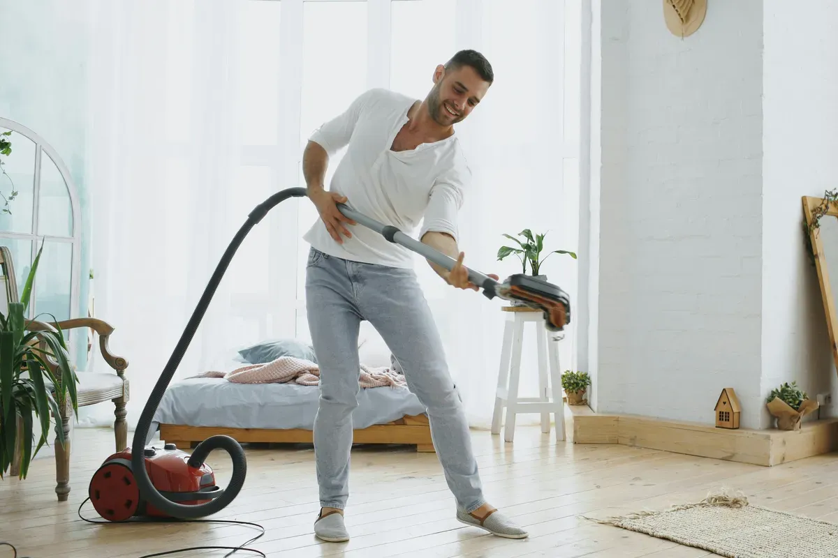 A person pushing an upright vacuum across a room floor